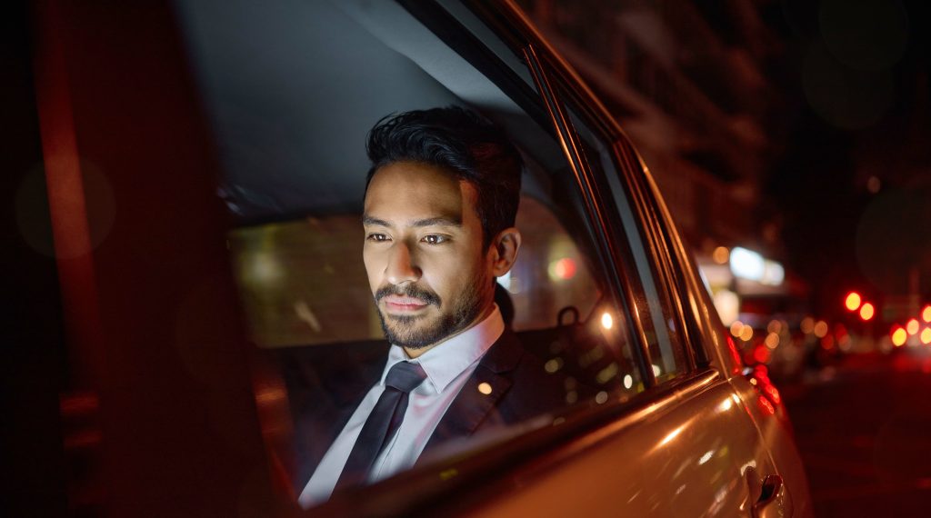 Businessman relaxing in the back seat of a luxury car during nighttime travel, illustrating comfort, productivity, and premium executive chauffeur service.