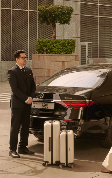 Chauffeur standing beside a Mercedes-Benz luxury sedan with travel luggage placed near the rear of the car.