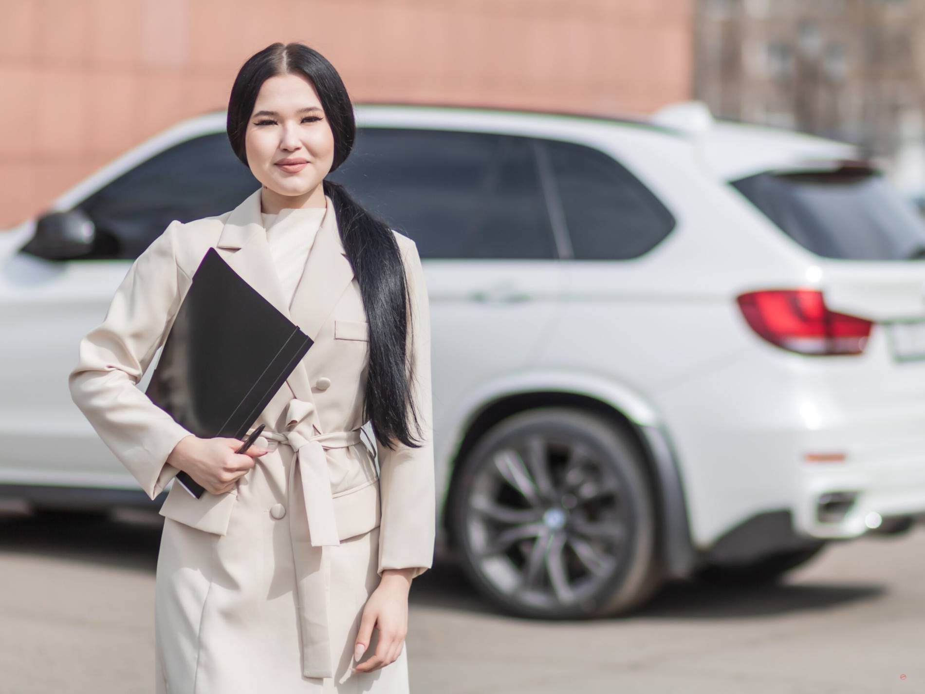 Professional chauffeur service representative standing in front of a white luxury SUV, holding a folder for premium car booking.
