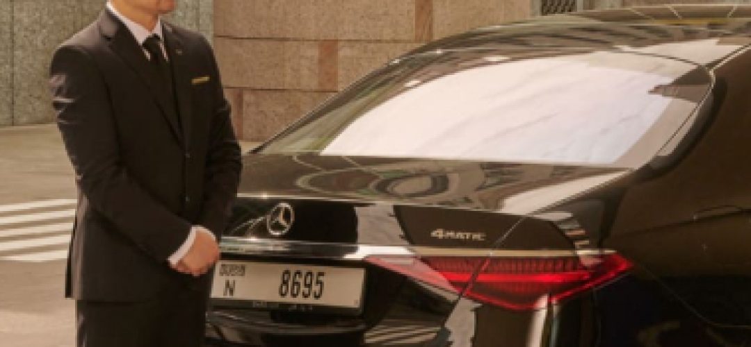 Chauffeur standing beside a Mercedes-Benz luxury sedan with travel luggage placed near the rear of the car.