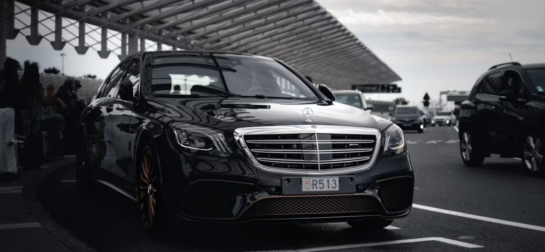 Luxury sedan parked at an airport terminal during passenger pickup.