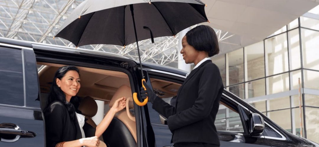ProRido chauffeur assisting passenger with umbrella at airport in rain luxury van